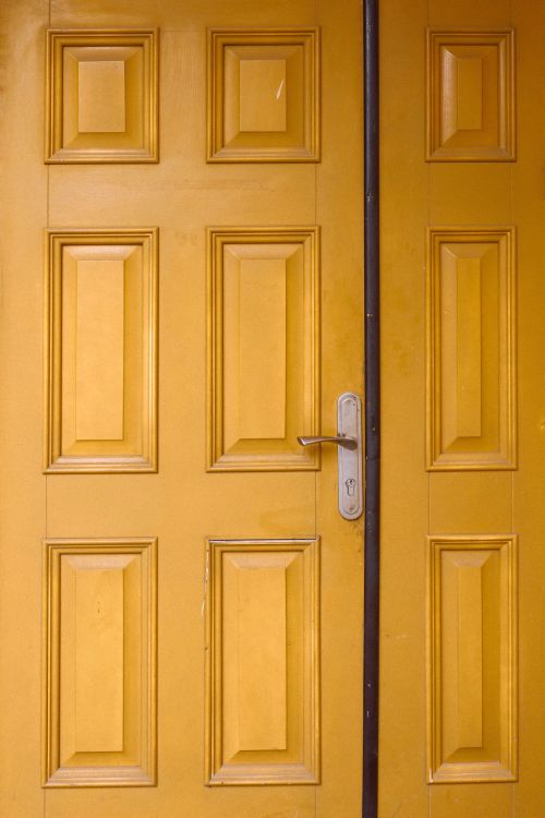 Free Vibrant yellow wooden door with panel details and a metal lock handle. Stock Photo