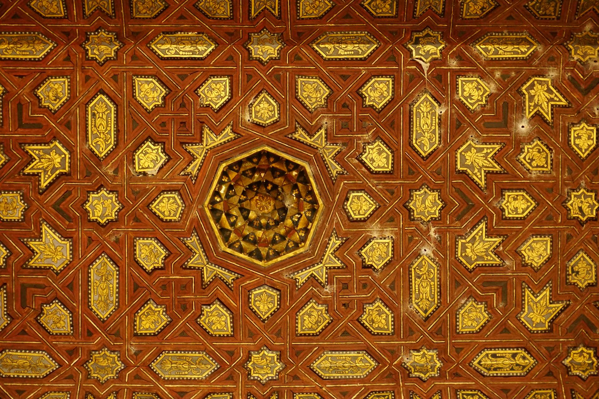 Detailed view of an ornate Moorish ceiling featuring complex geometric patterns in rich browns and golds.