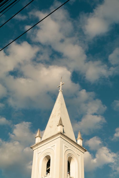 Free Charming white church steeple extending into a bright, cloud-dappled sky. Stock Photo