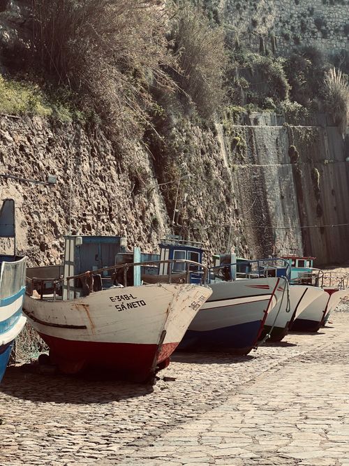 Free A scenic view of rustic fishing boats lined up on a cobblestone path against a cliff. Stock Photo
