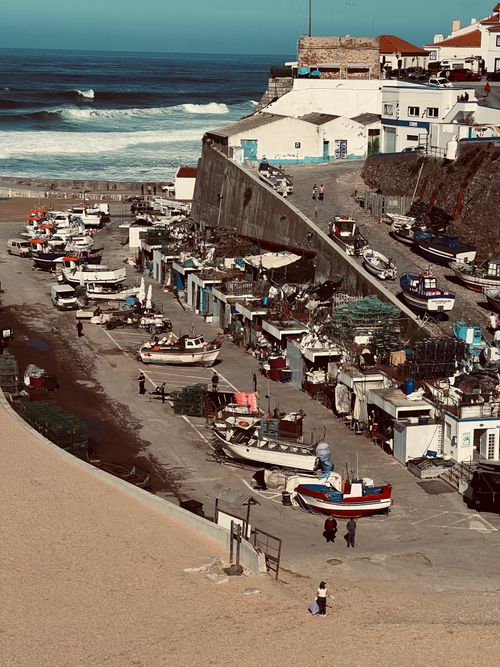 Free Aerial view of a charming coastal fishing village with boats docked and waves crashing in the ocean. Stock Photo