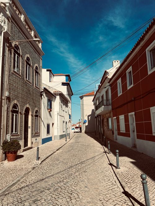 Free Sunlit cobblestone street between historic European homes in a Mediterranean village. Stock Photo