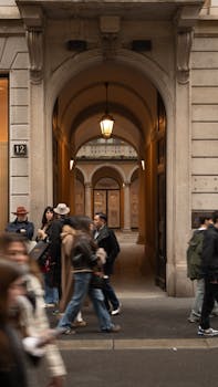A stylish urban street scene with people walking past a grand architectural archway.