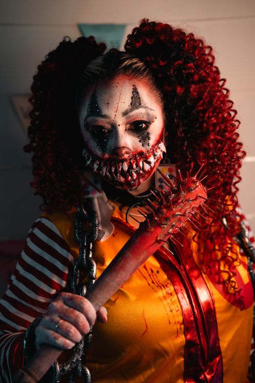 Free Intense portrait of a person in clown makeup with spiked bat, rich in detail and mood. Stock Photo