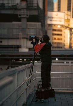 A determined photographer capturing cityscape at sunset, standing on equipment for height.