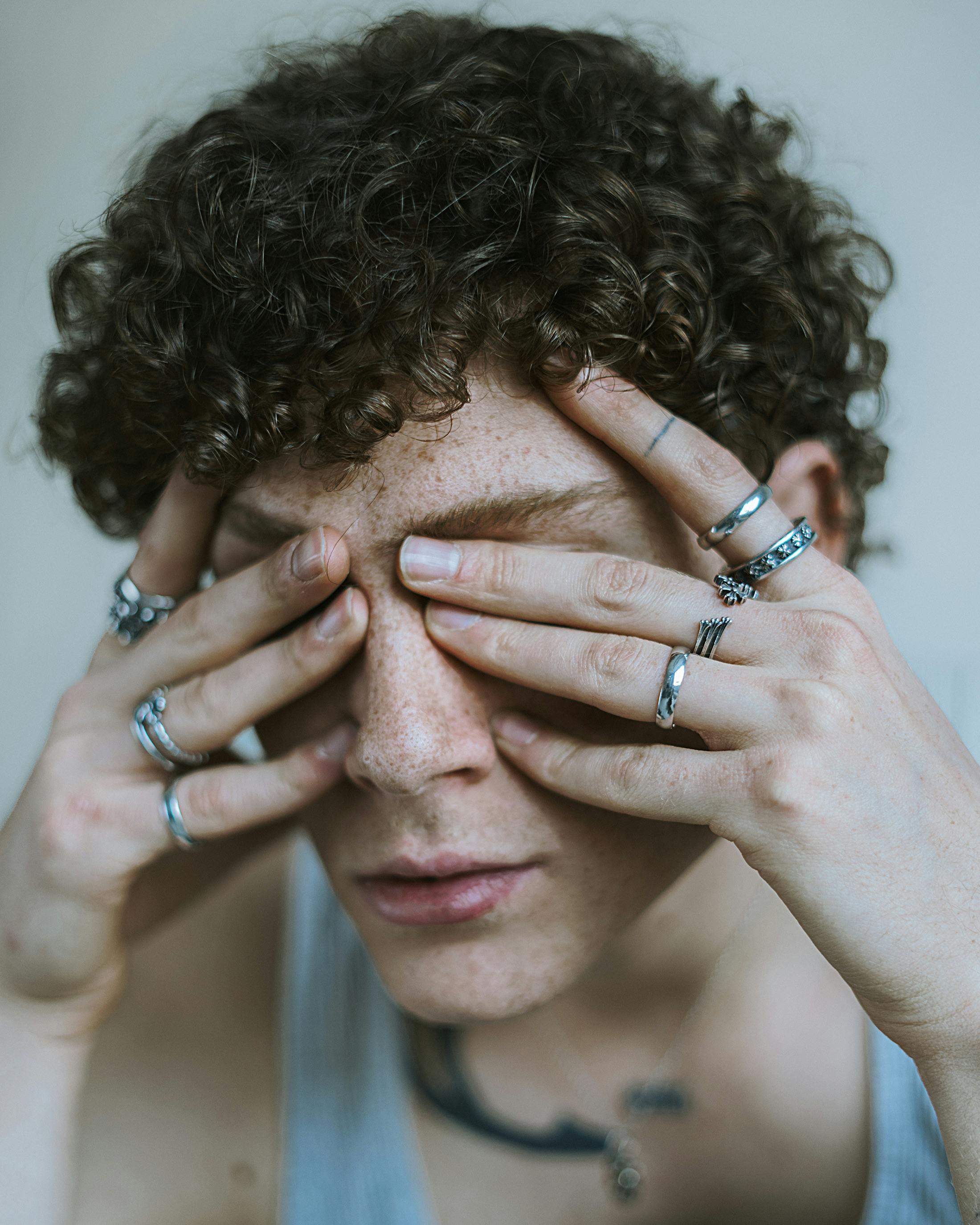Young adult with curly hair wearing multiple rings, covering face. Artistic portrait with a vintage mood.