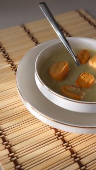 A delicious creamy soup with croutons served in a white bowl on a bamboo mat, perfect for cozy dining.