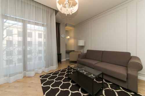 Free Bright modern living room featuring a brown sofa, chandelier, and large window with sheer curtains. Stock Photo