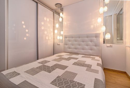 Free Modern bedroom with elegant lighting, featuring quilted bed and glass wall decor. Stock Photo