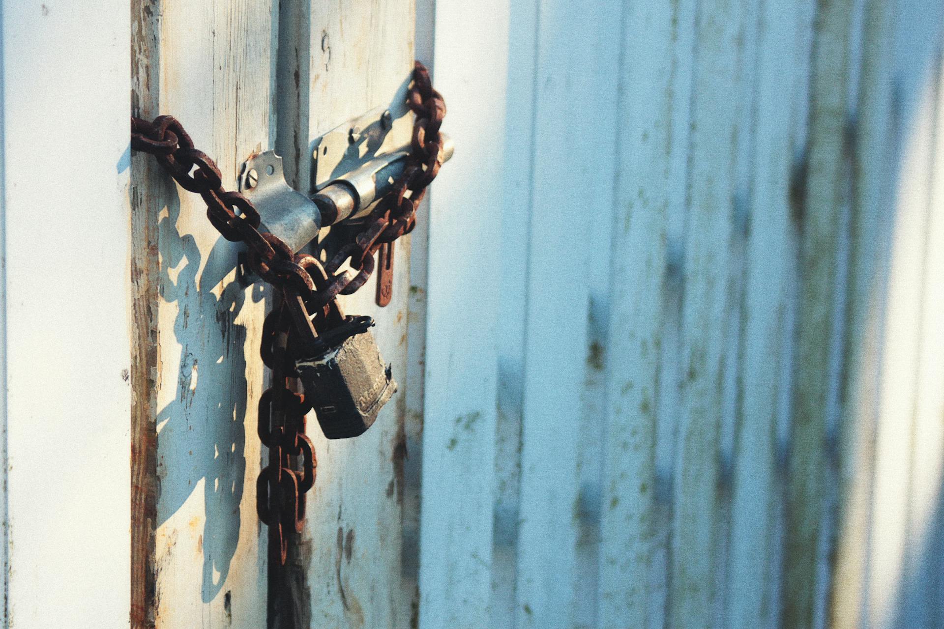 Close-up of a rusty chain and lock securing a weathered wooden door, capturing a rustic charm.