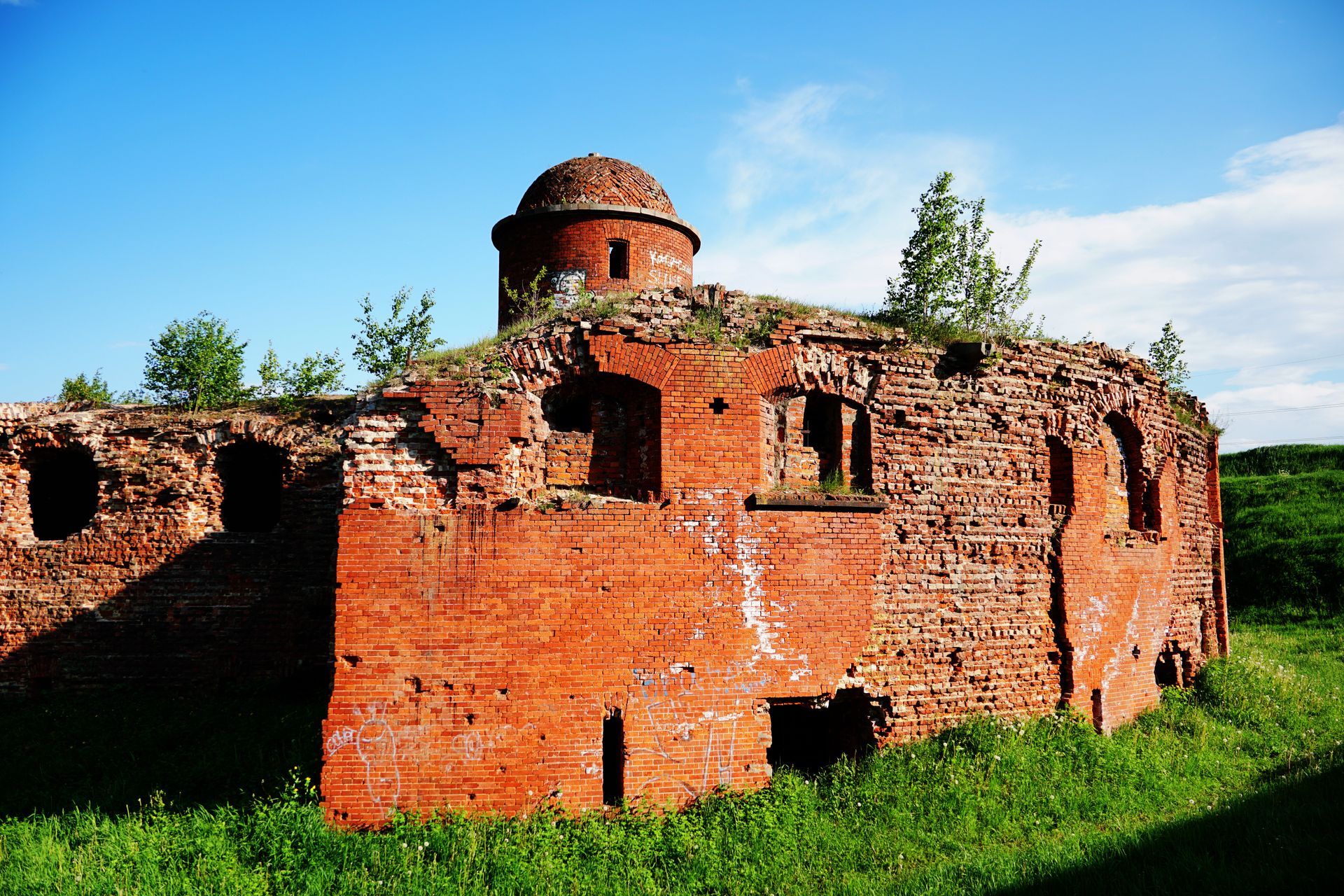 Historic red brick fort ruins with greenery, under a clear blue sky.