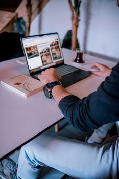 A person using a laptop in a cozy indoor setting with a book and tea.