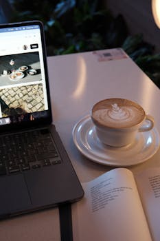 Warm cafe ambiance with laptop, latte, and open book.