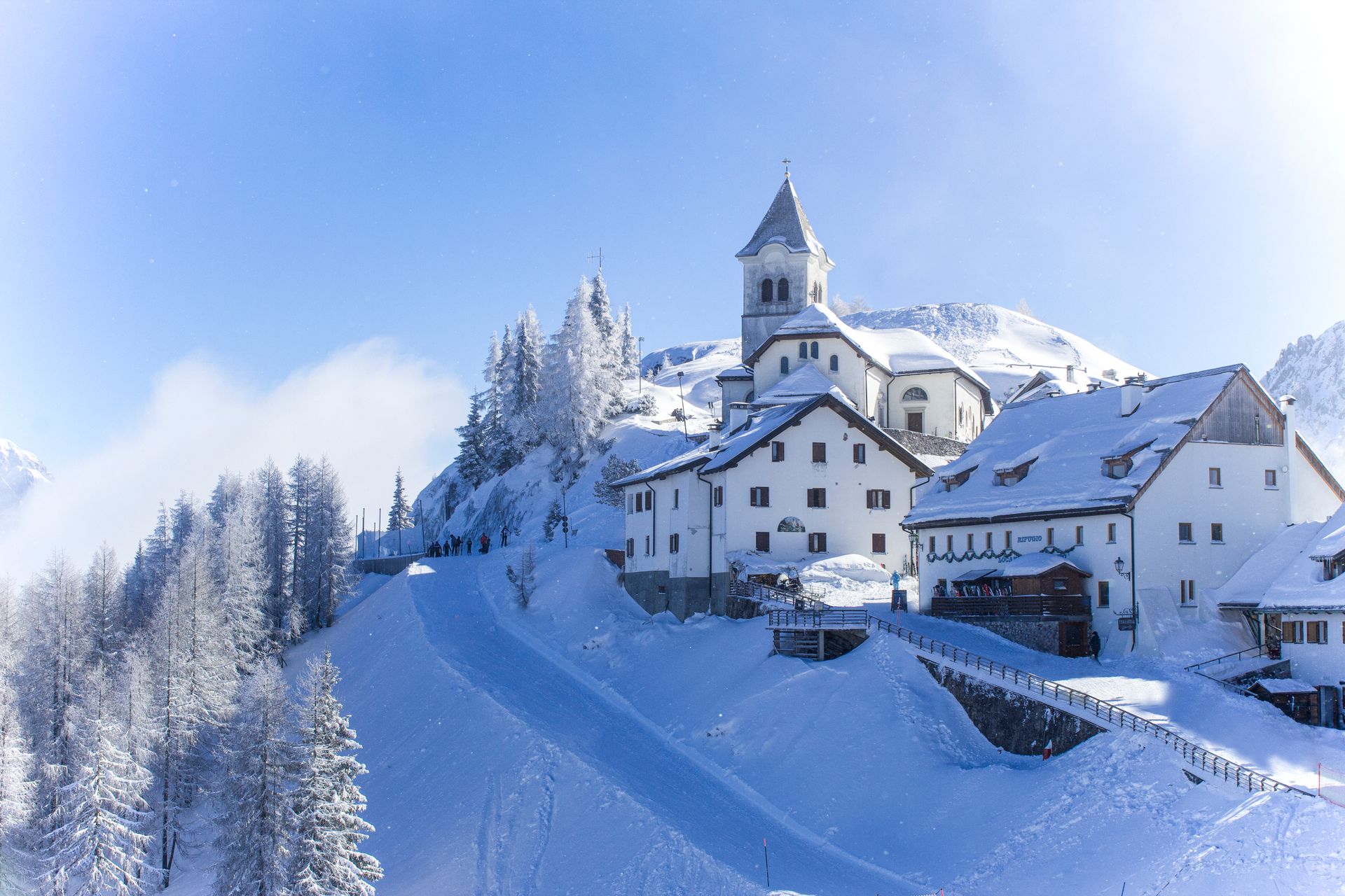 Snow-covered church and village in Camporosso, Italy, under bright winter sky.