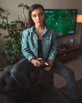 Young woman in denim jacket playing video games indoors with modern setup.
