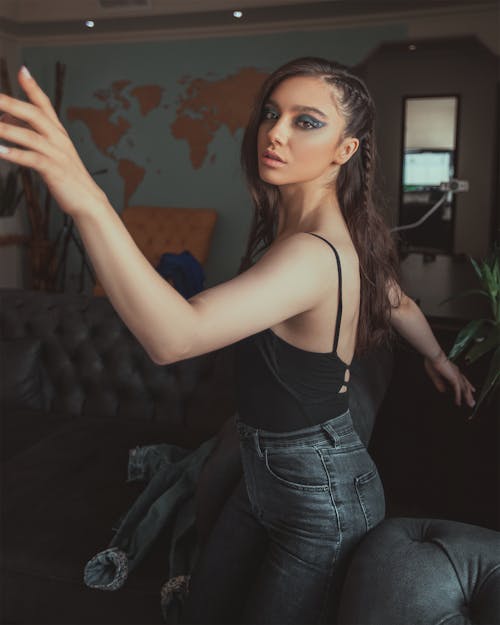 Photo of Woman in Black Tank Top and Jeans Sitting on Arm of Sofa Posing