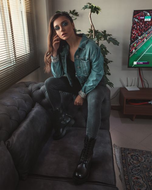 Free Stylish young woman sitting on sofa, expressing modern fashion in denim jacket and boots. Stock Photo