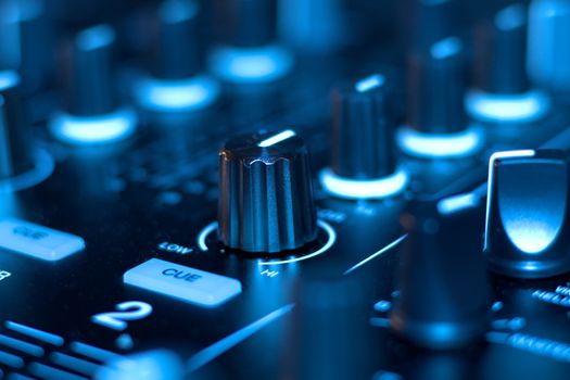 Detailed view of DJ mixer controls with blue lighting, perfect for electronic music themes.