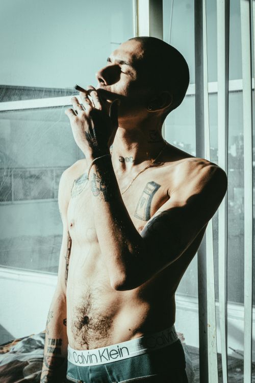 Free Tattooed man smoking indoors in sunlight. Moody and artistic capture. Stock Photo