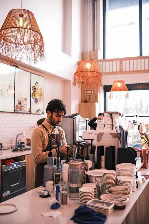 Free Barista preparing coffee in a warmly lit modern cafe with wicker lighting. Stock Photo