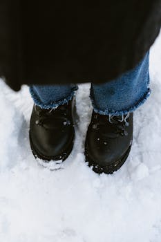 A pair of black winter boots standing in snow, showcasing snowy terrain and winter fashion.