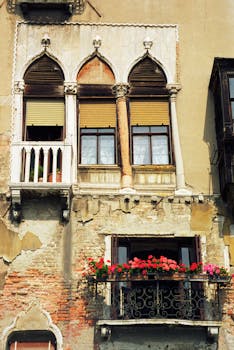 Historic Venetian building facade with ornate windows and vibrant flower boxes in Venice, Italy.