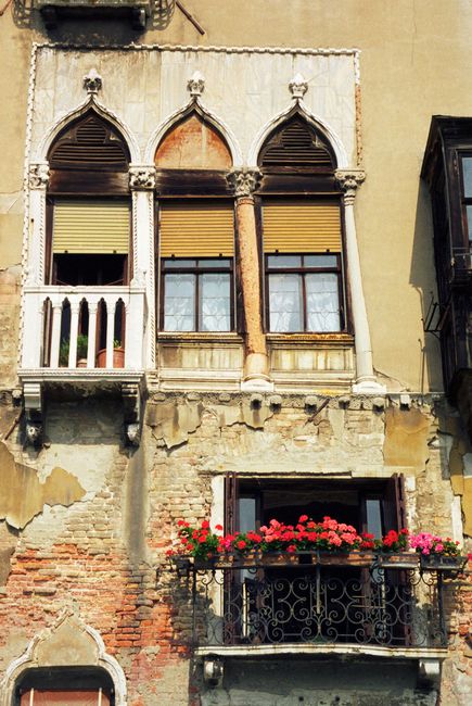 Historic Venetian building facade with ornate windows and vibrant flower boxes in Venice, Italy.