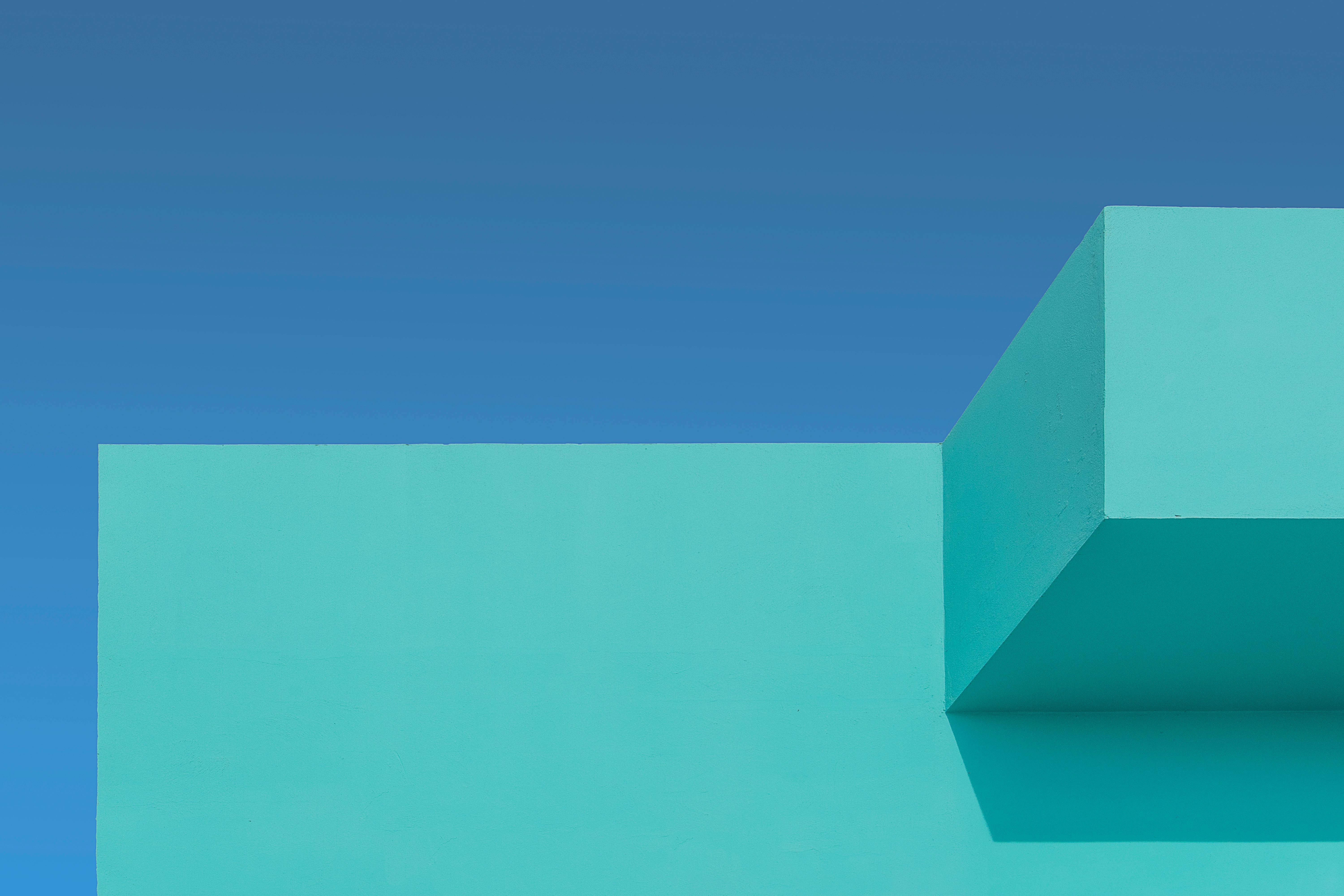 Kostnadsfria En minimalistisk turkos byggnadsfasad mot en levande blå himmel, som visar upp geometrisk arkitektur. Stock foto