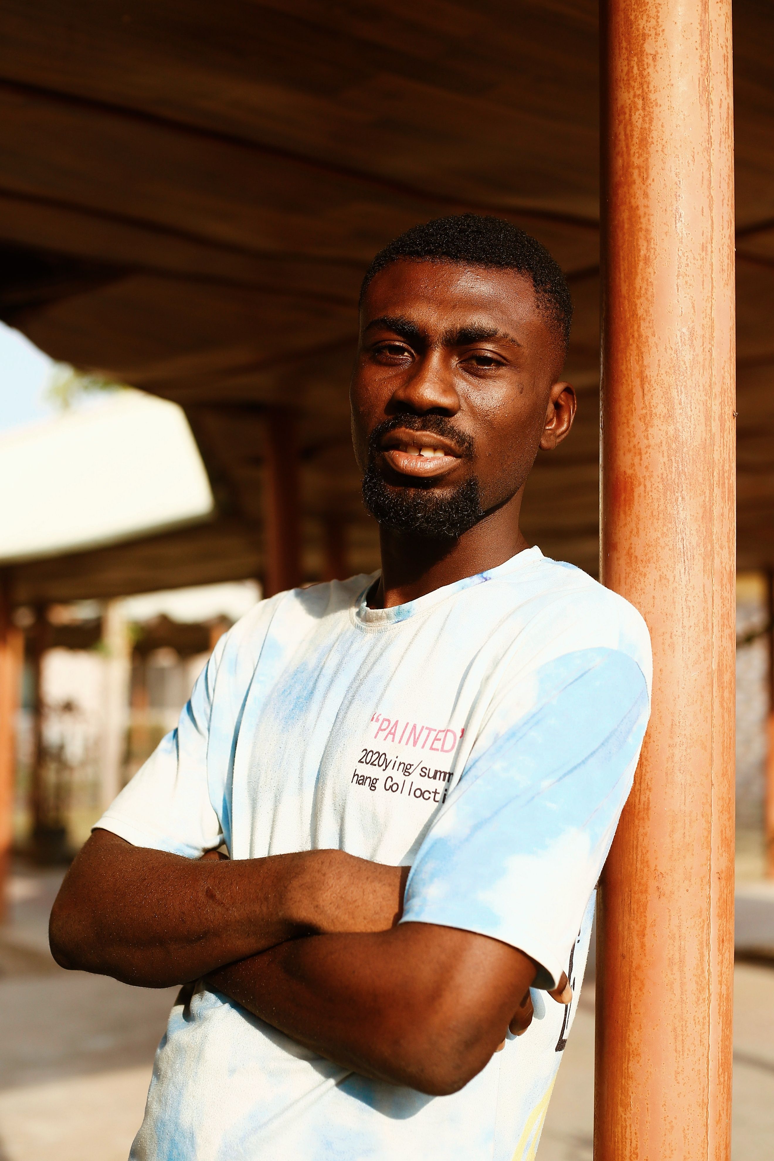 Confident man standing with arms crossed outdoors on a sunny day in Nigeria.