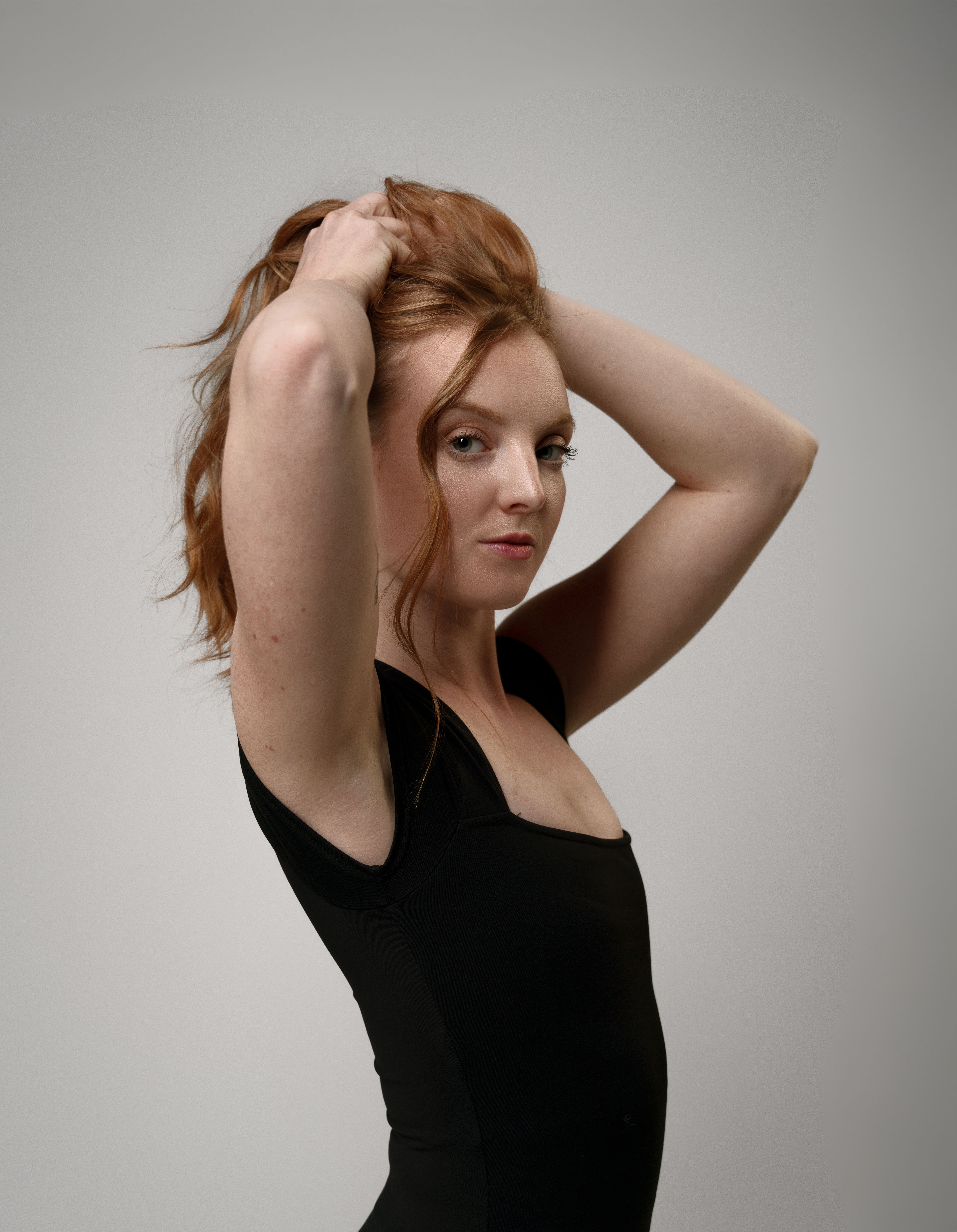 Studio portrait of an elegant woman with ginger hair posing against a neutral background.