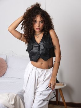 Fashionable woman with curly hair poses indoors in a modern outfit, exuding confidence.