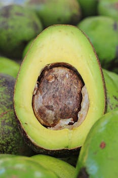 Close-up of a ripe avocado sliced in half, revealing its stone, amidst other avocados.