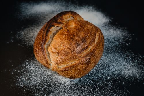 Free A rustic artisanal bread loaf on a dark background sprinkled with flour. Stock Photo