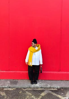 Fashionable portrait of a man with a bold yellow scarf standing against a vibrant red wall.