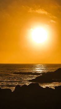Stunning sunset over rocky coast with vibrant orange hues and shimmering ocean.