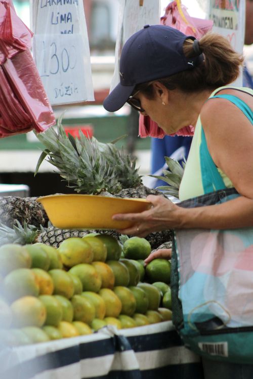Free A woman selects fresh pineapples at a vibrant outdoor market fruit stand. Stock Photo