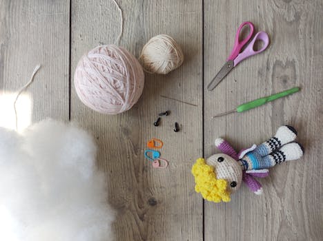 A flat lay image of crochet supplies featuring yarns, scissors, needles, and a handmade doll on wooden background.