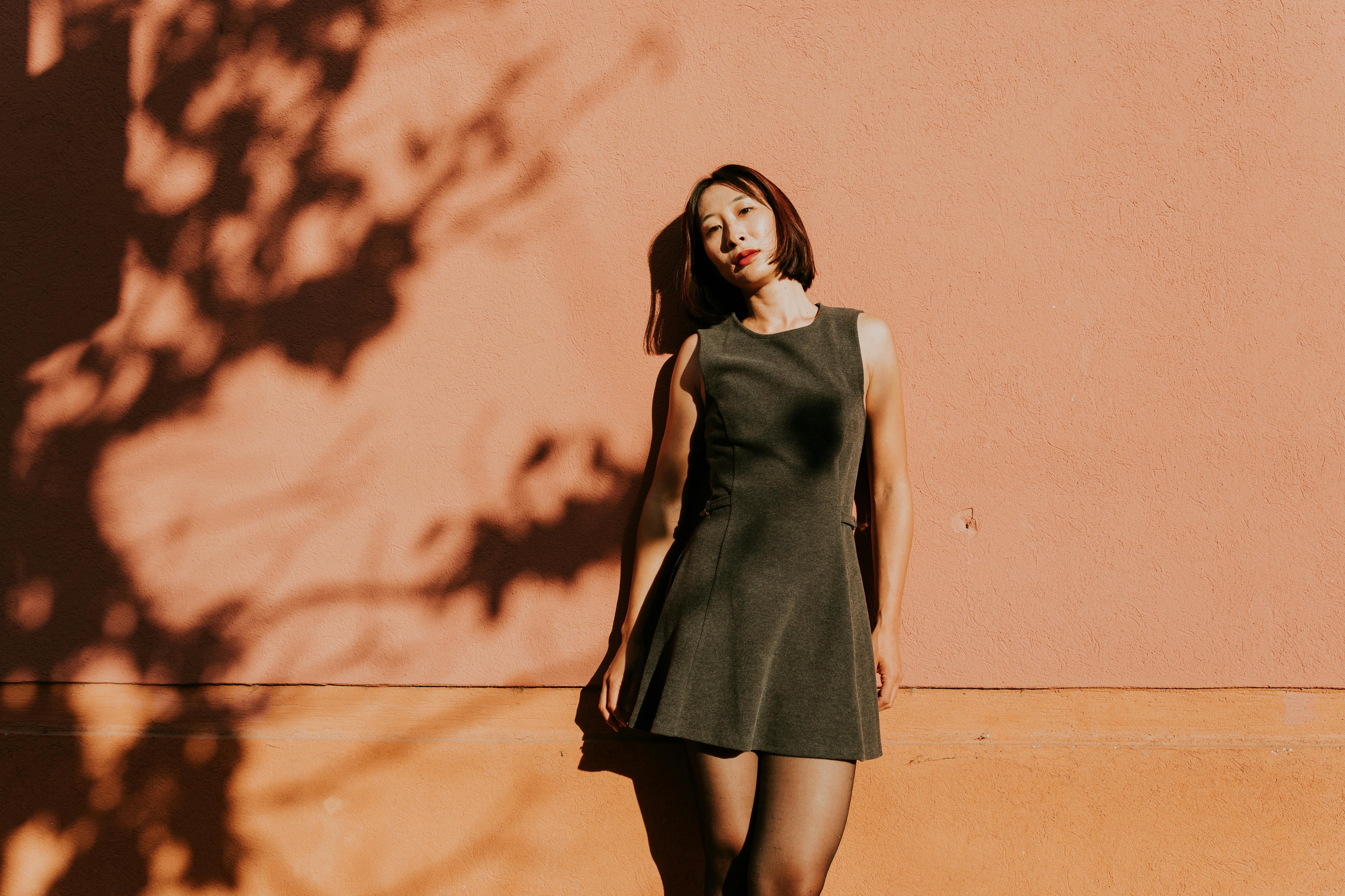 Stylish woman in a dress posing by a sunlit wall, casting shadows.