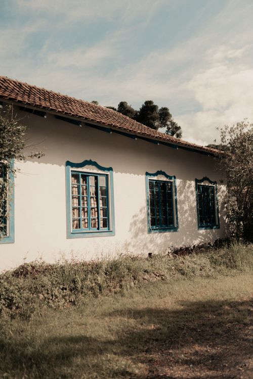 Free A rustic white house with blue window trim in a serene countryside setting. Stock Photo