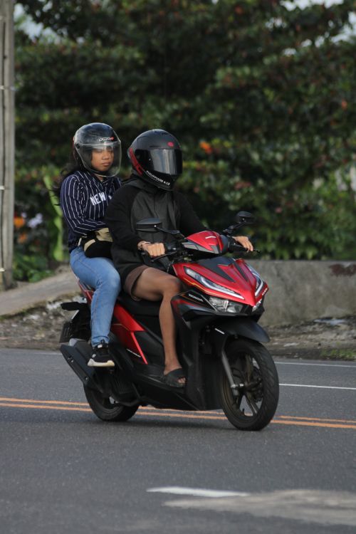 Free Two people wearing helmets ride a red motorcycle on a road. Stock Photo
