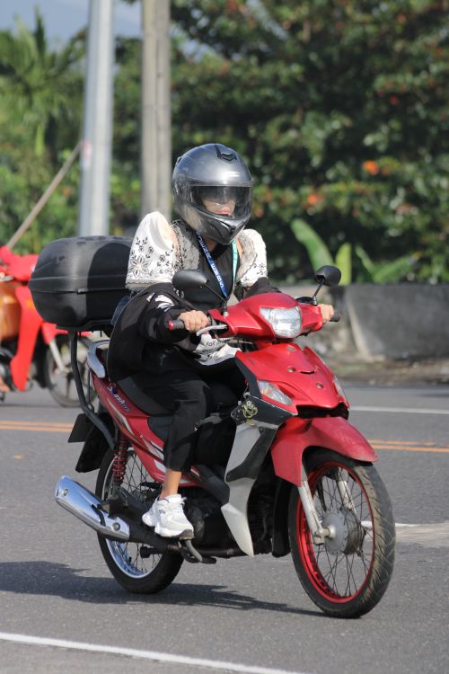 Free A person in protective gear rides a red scooter outdoors on a sunny day. Stock Photo