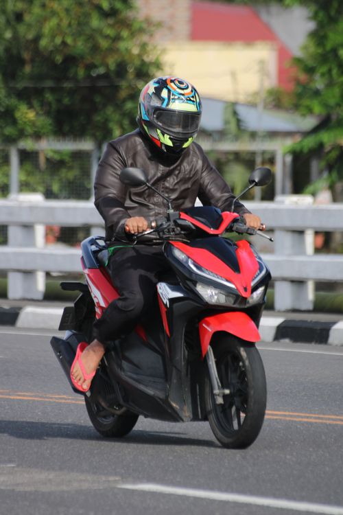 Free Motorcyclist in helmet riding a red scooter on a sunny urban road. Stock Photo