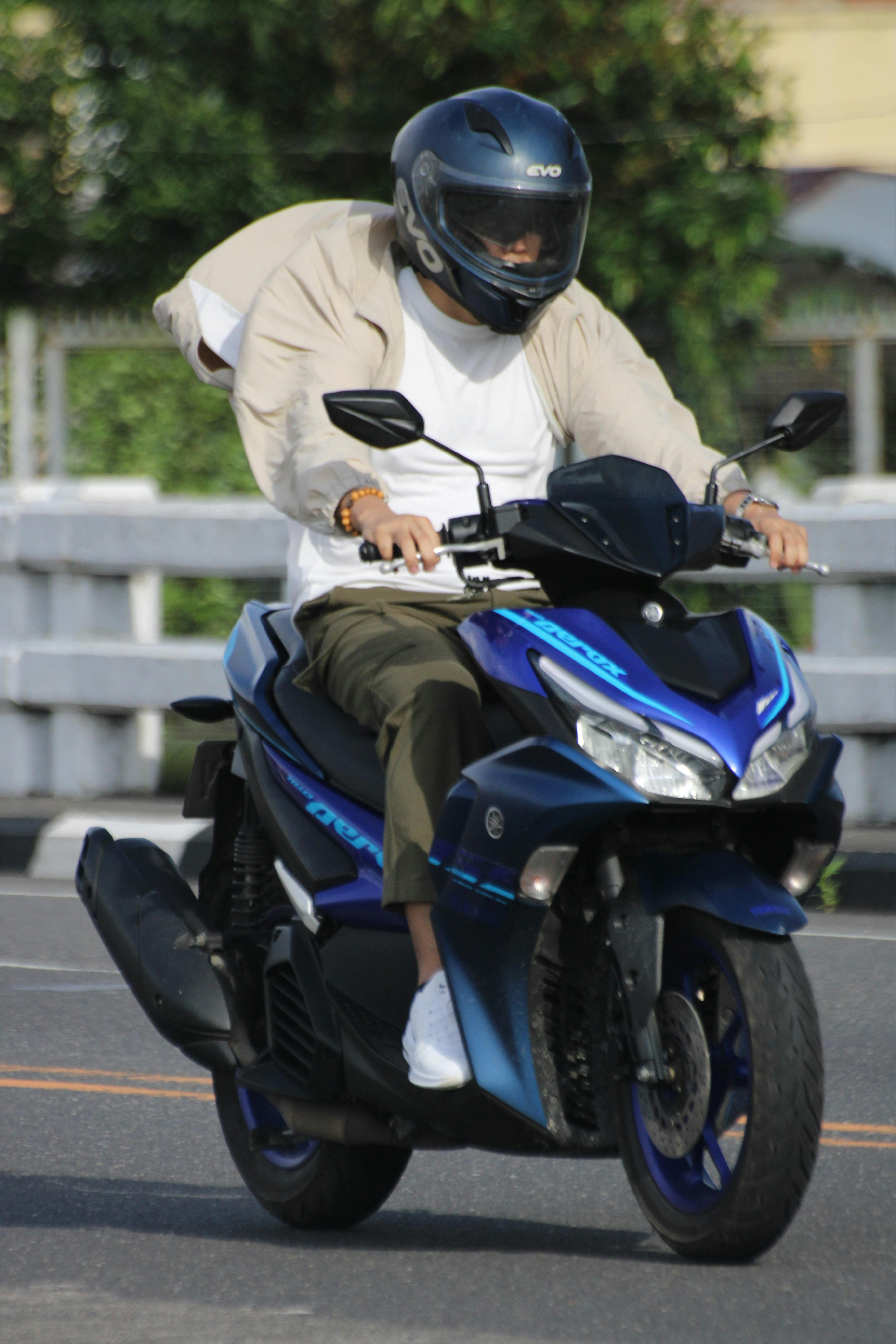 Free Adult male on a blue motorcycle cruising through urban streets. Stock Photo