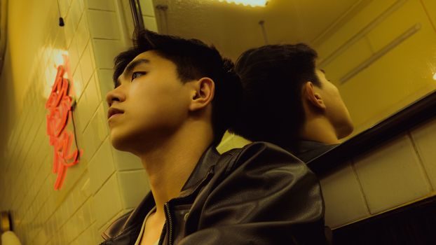 A reflective portrait capturing a young man by a mirror in a warmly lit room.