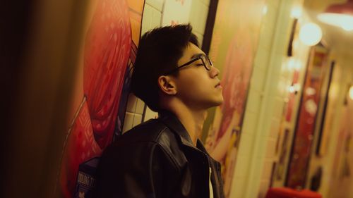 Free A man in a leather jacket leans against a colorful wall, lost in thought. Stock Photo