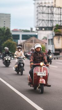 Man riding a classic Vespa scooter down a busy street in West Java, Indonesia.