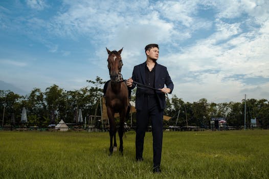 A stylish man in a suit holding a horse in a picturesque outdoor setting.