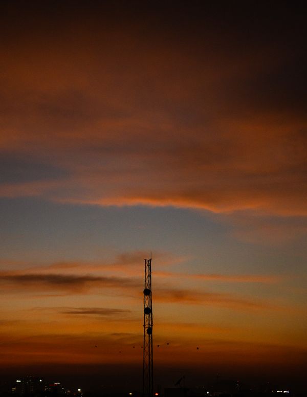 Silhueta de torre de telecomunicações contra um vibrante céu do pôr do sol de Bengaluru, capturando a hora dourada da cidade.