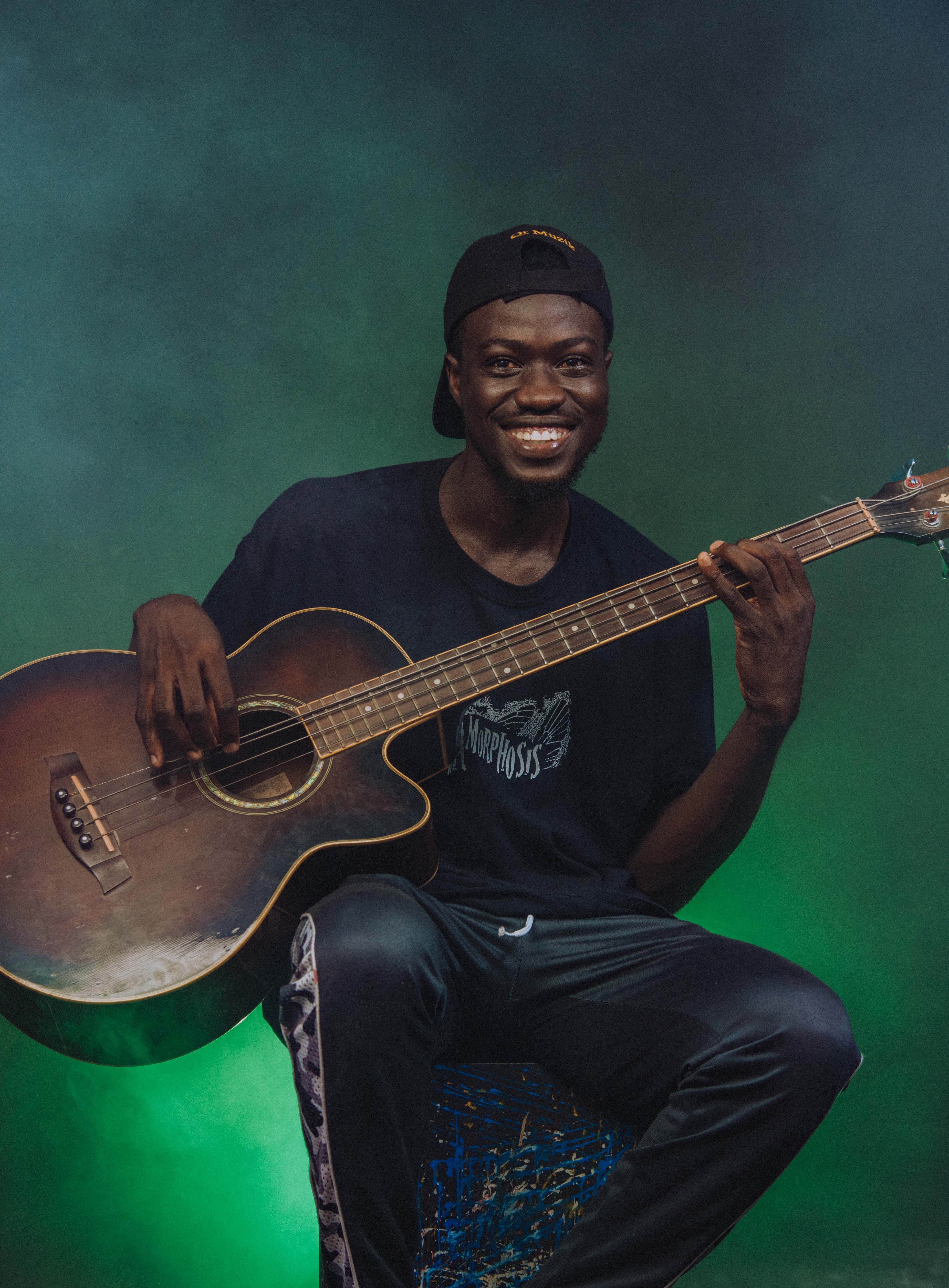 A cheerful young musician poses with an acoustic guitar in a vibrant studio setting.