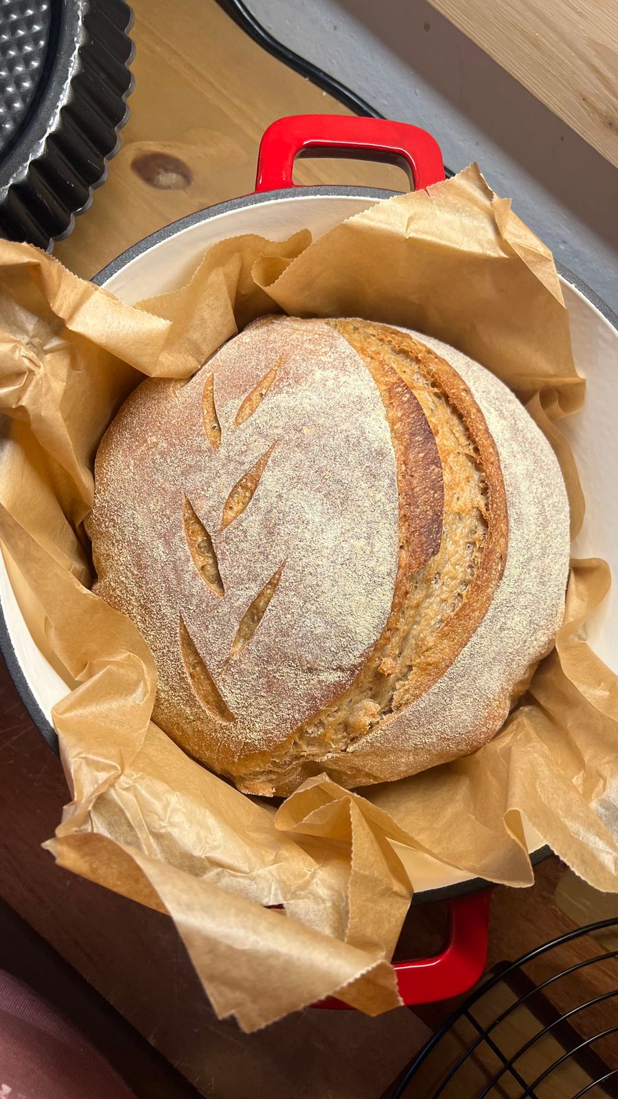 Rustic sourdough bread fresh from the oven, beautifully scored, in a red Dutch oven